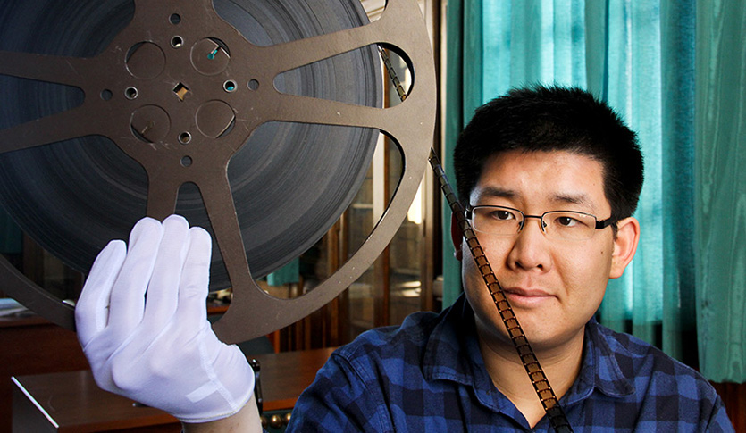 Dr. Joseph W. Ho examines an old film reel that he holds with a gloved hand.
